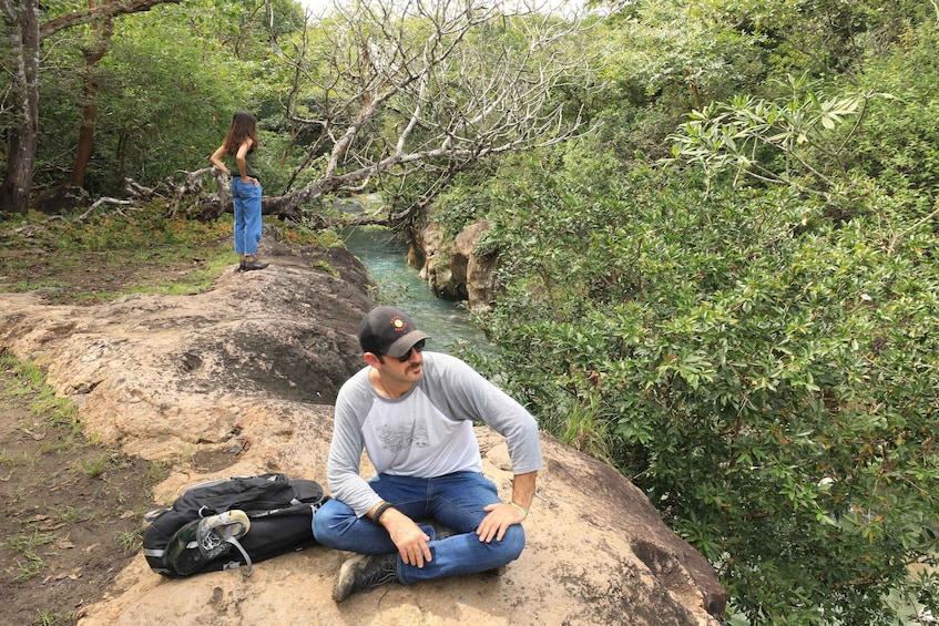 A man sitting on a rock by a river in a forest. 4