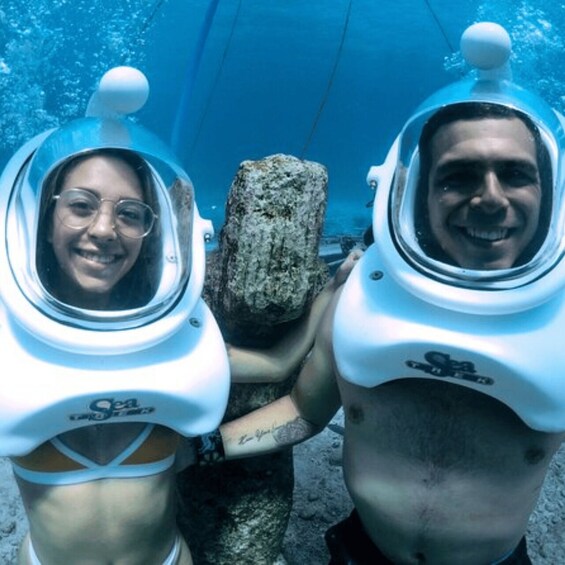 Two people in scuba diving gear underwater near a rock. 5