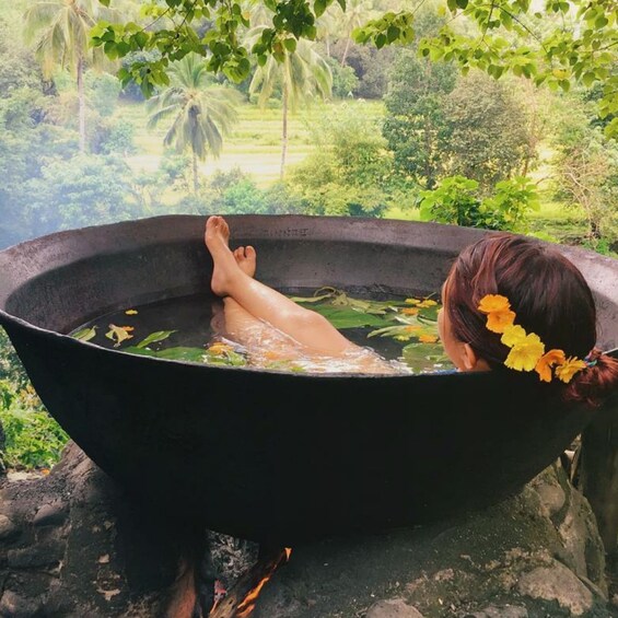 A person relaxing in a large black tub outdoors surrounded by lush greenery. 4