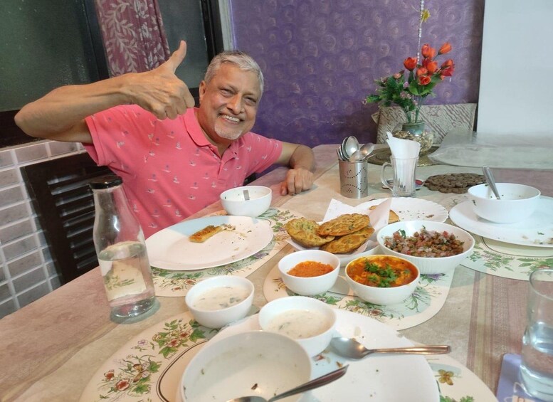 A man giving a thumbs-up at a table with various dishes, including bowls of soup and a plate of bread. 3
