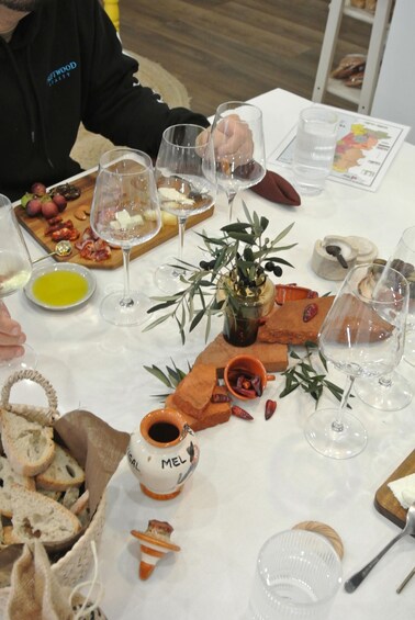 A table with wine glasses, cheese, olives, bread, and a small vase labeled 'MEL.' 3