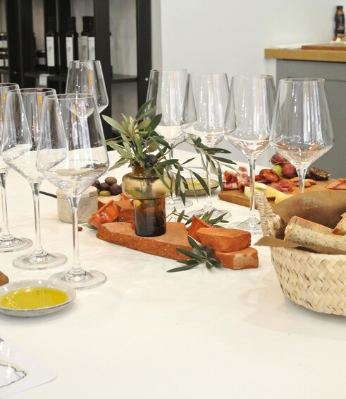 A table with wine glasses, a plant, cheese, bread, and olives. 1