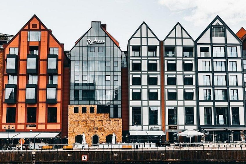 A row of modern buildings with distinct architectural styles, including a red building with a unique facade and a glass building with a logo. 3