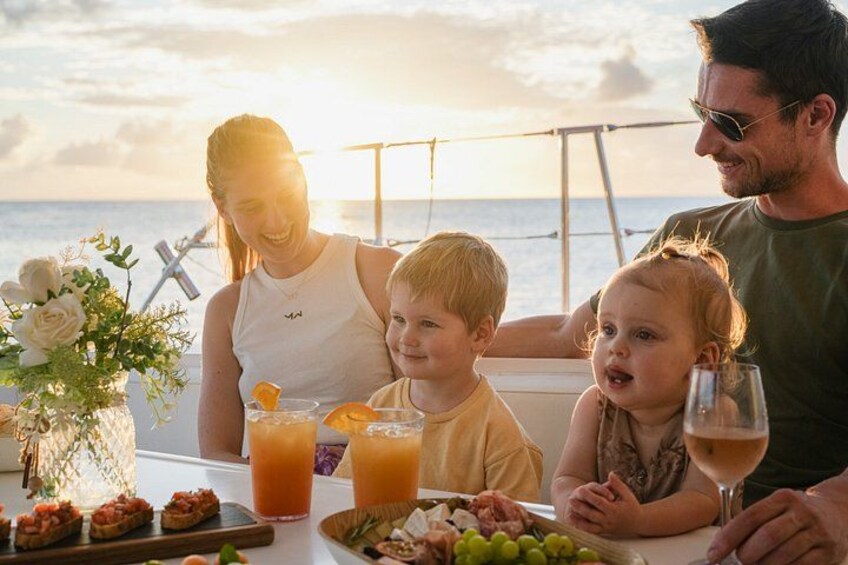 Een gezin eet aan een tafel met eten en drinken, met uitzicht op zee. 3