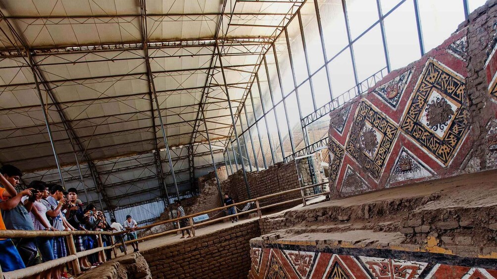 An archaeological site with a partially uncovered structure, visitors observing the site, and intricate wall decorations. 2