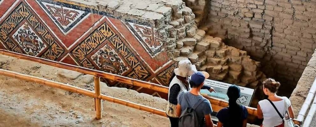 A group of people observing an ancient mosaic and a brick structure at a historical site. 1