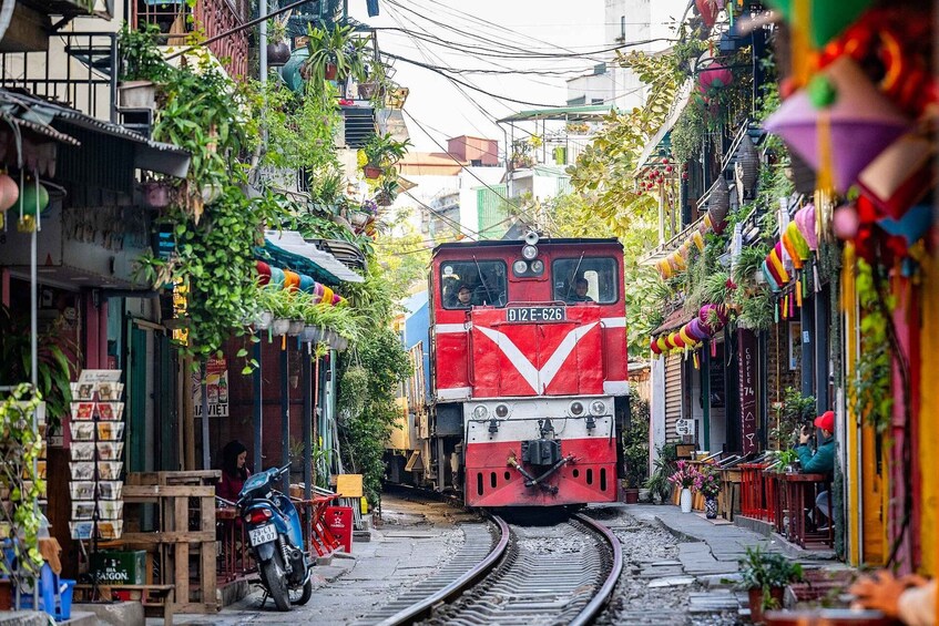 A red train on tracks in a narrow street with buildings on either side. 1