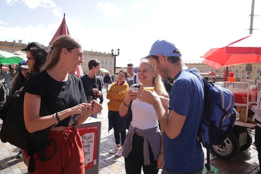 People standing outdoors, some holding drinks, with a food cart in the background. 2