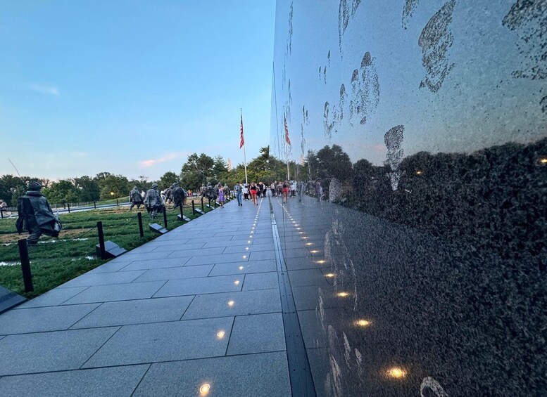 A memorial wall with engraved names, a paved walkway, and a grassy area with statues. 1