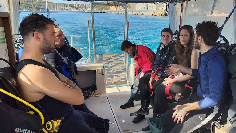 A group of people on a boat, some wearing diving gear, with a view of the sea and a dock in the background. 3
