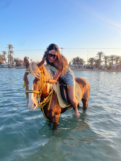 A person riding a horse in shallow water with palm trees in the background. 4