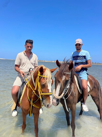 Two people riding horses in shallow water. 2