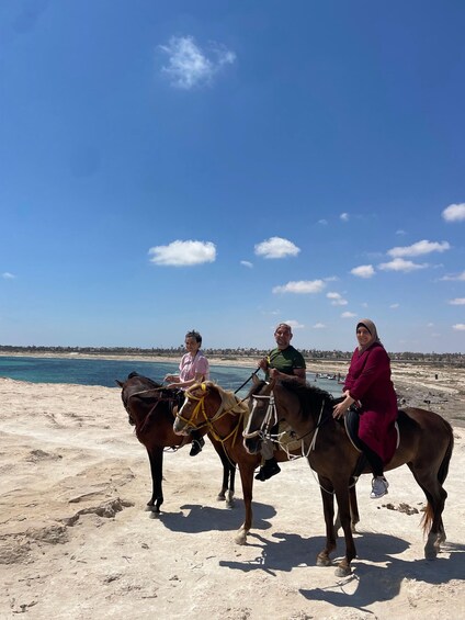 Three people riding horses on a beach with a clear sky. 5