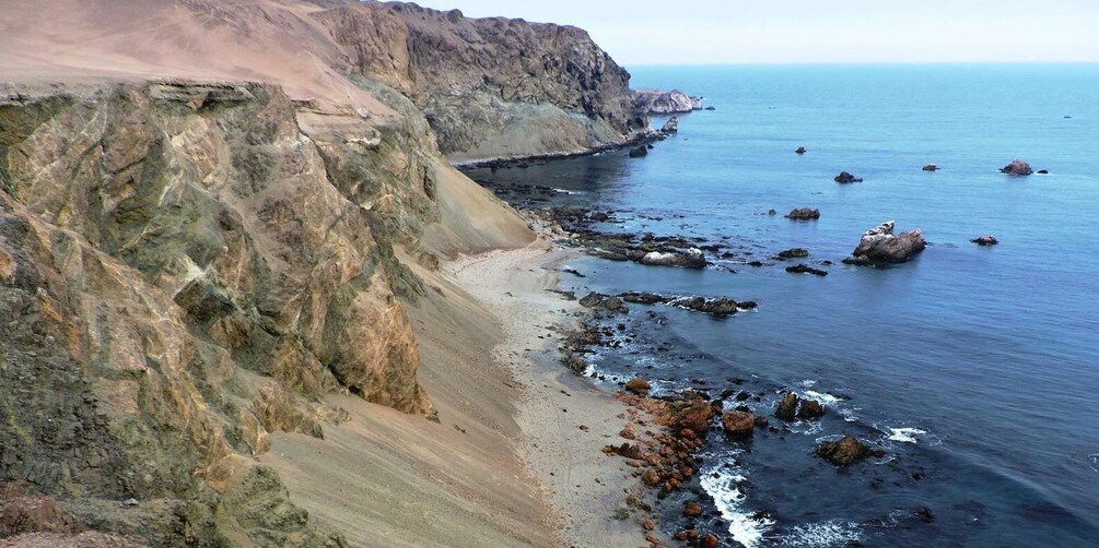A coastal landscape with a steep cliff, sandy beach, and scattered rocks near the water's edge. 2
