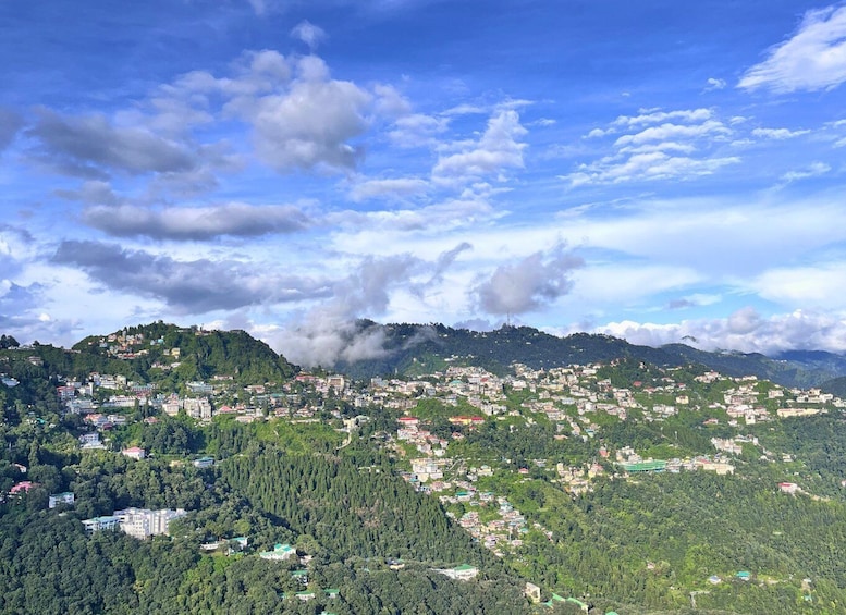 A mountainous landscape with scattered buildings, dense forests, and a partly cloudy sky. 4