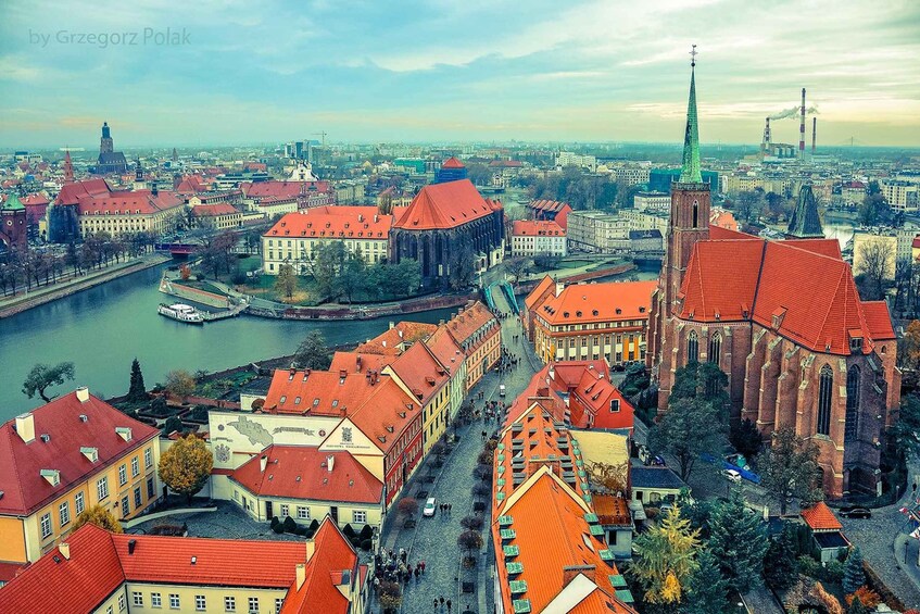 A cityscape with red-roofed buildings, a river, and a prominent church with a tall spire. 1