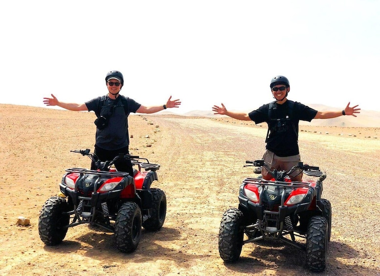 Two people standing on ATVs in a desert with their arms outstretched. 2