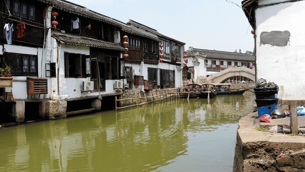 A traditional Chinese waterway with wooden buildings, a stone bridge, and boats. 5