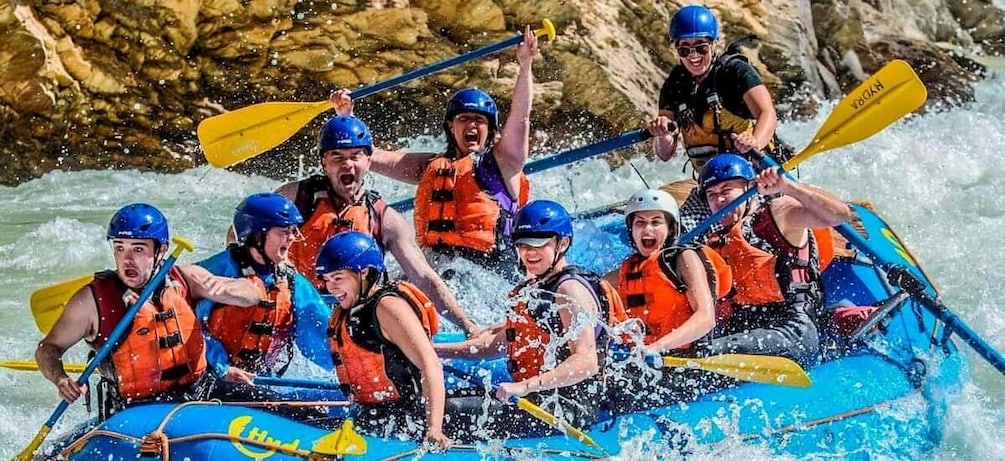 A group of people in a blue raft navigating through white water rapids. 1