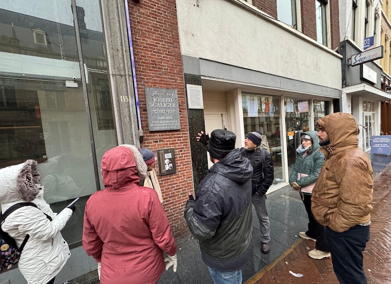 A group of people standing outside a building with a plaque and a signboard. 3