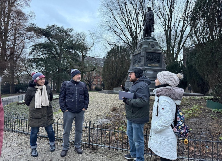 A group of people standing near a statue in a park with leafless trees and a fence in the background. 5