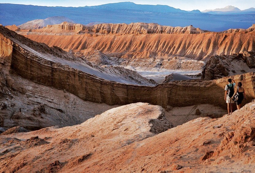 Una persona de pie sobre un afloramiento rocoso con vistas a un extenso paisaje desértico con formaciones rocosas estratificadas. 1