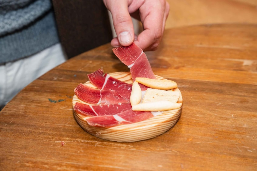 A wooden board with sliced cured meat and crackers. 3