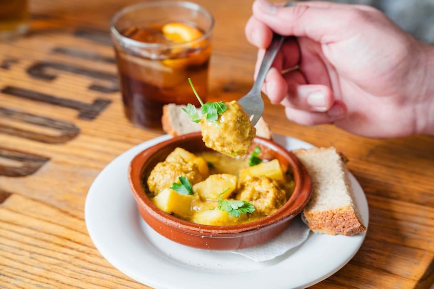 A bowl of meatballs with potatoes and a glass of tea on a wooden table. 1