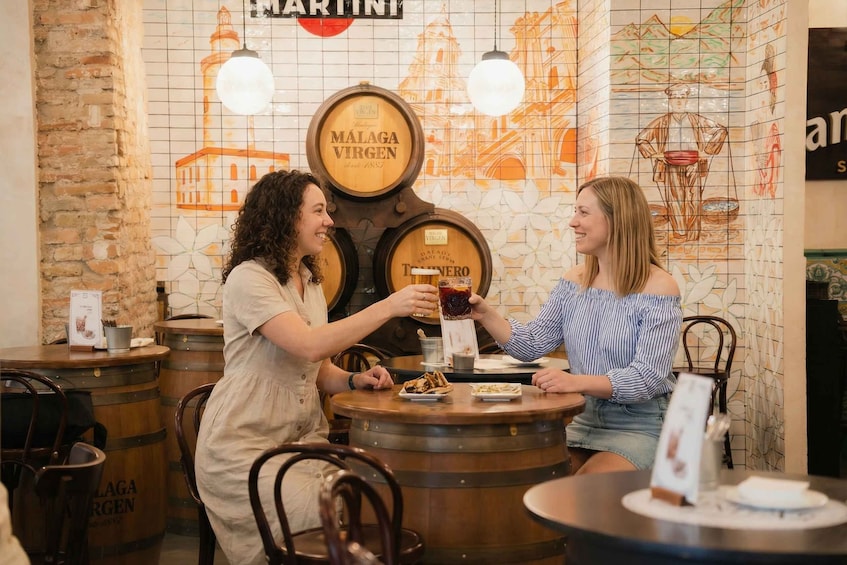 Two people toasting with drinks at a bar with wooden barrels and a mural in the background. 4