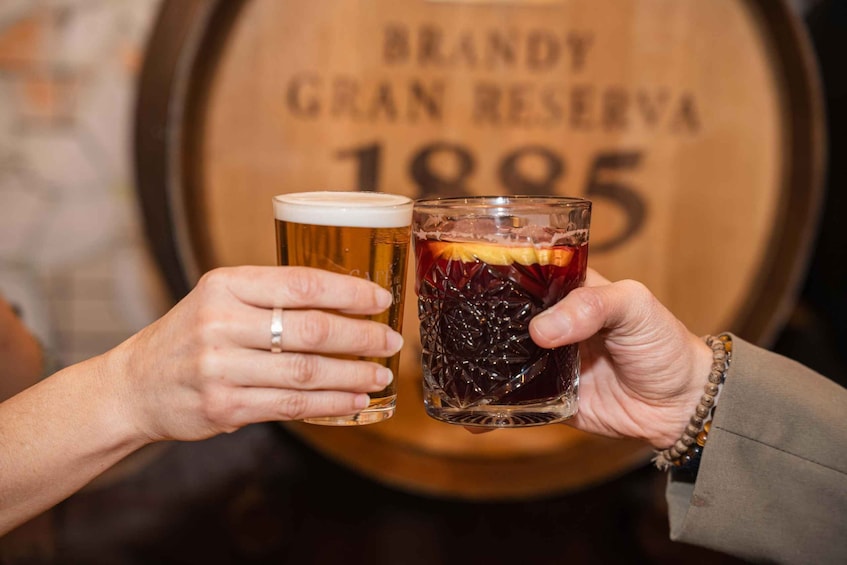 Two hands holding a beer glass and a cocktail glass with a fruit garnish. 5