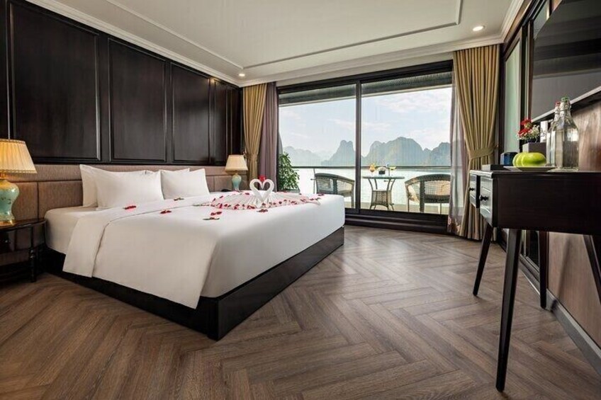 A hotel room with a large bed, wooden flooring, a balcony with a view of the sea, and a desk with a lamp. 3