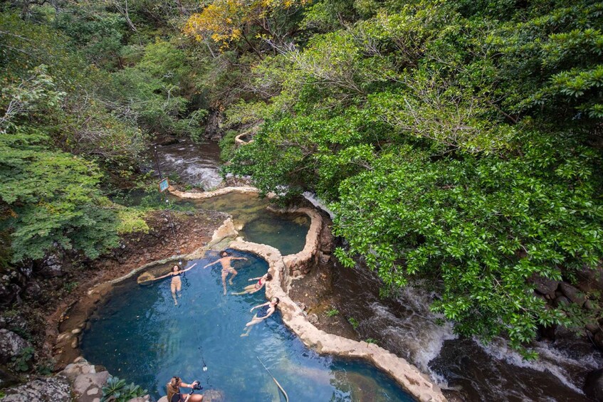 A natural hot spring surrounded by lush greenery and a flowing stream. 2