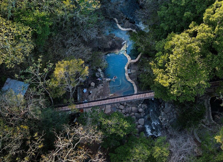 An aerial view of a natural pool surrounded by dense forest, with a wooden bridge crossing over the water. 4