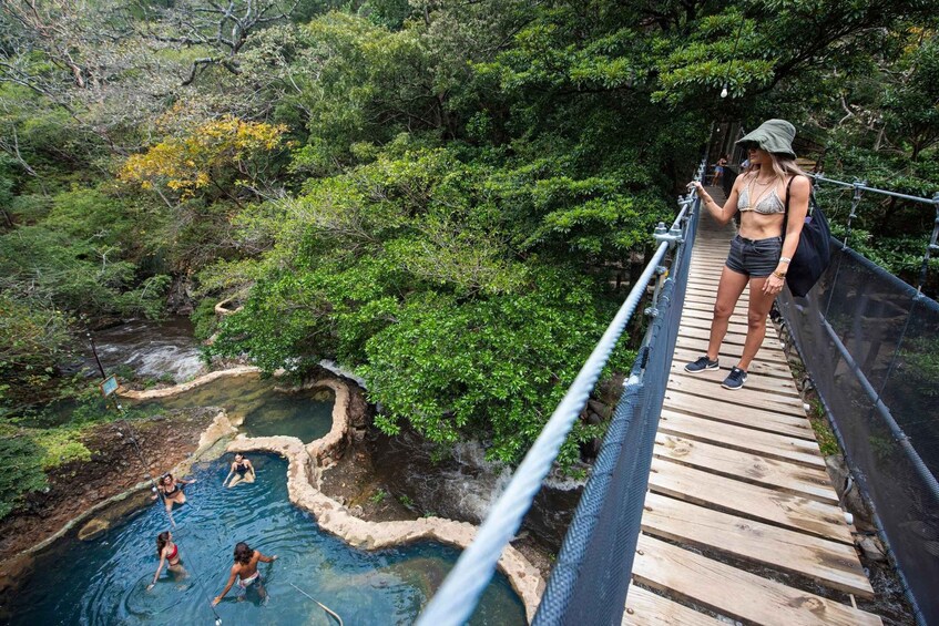 A wooden bridge over a hot spring surrounded by lush greenery. 1