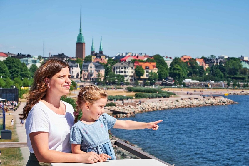 A woman and a child pointing at a cityscape with a prominent tower and a waterfront. 2