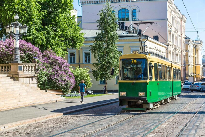 A green and yellow tram on tracks, a person walking on the sidewalk, and a building with arched windows in the background. 3