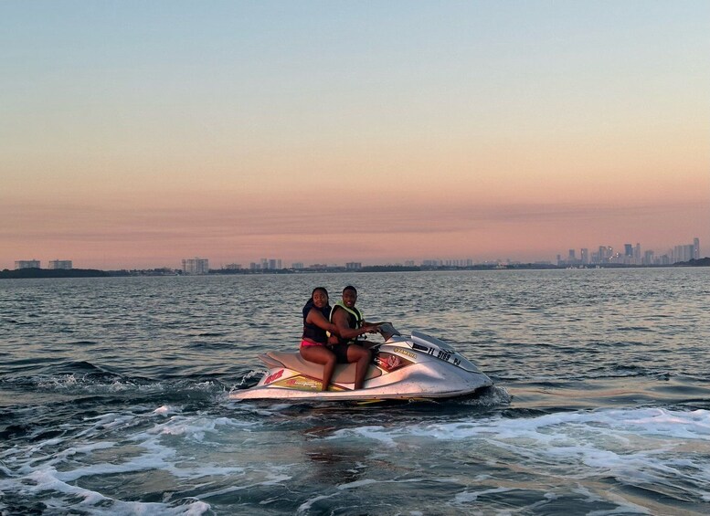 Two people on a jet ski in the water with a city skyline in the background. 2