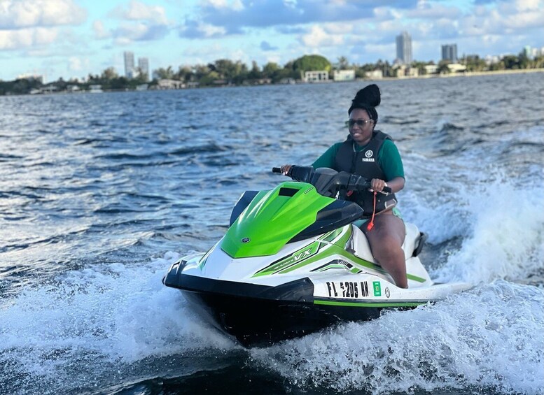 A person riding a green and white Yamaha jet ski on a body of water with a city skyline in the background. 1