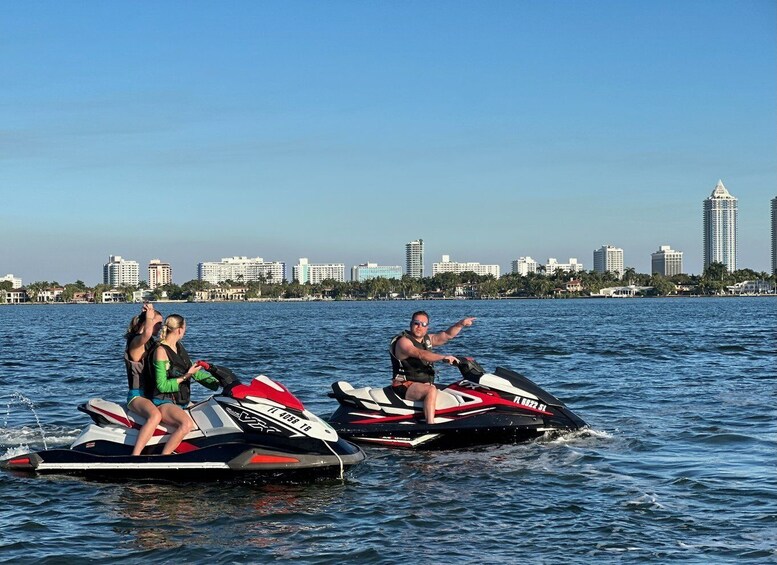 Three people jet skiing on a body of water with a city skyline in the background. 4