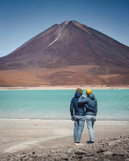 Two people standing on a beach facing a mountain. 4