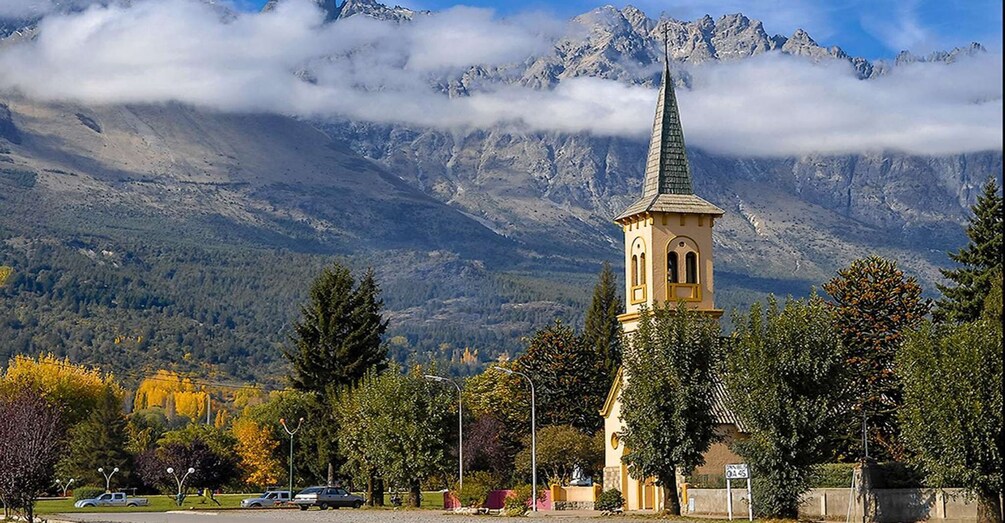 A church with a spire, surrounded by trees and mountains. 3
