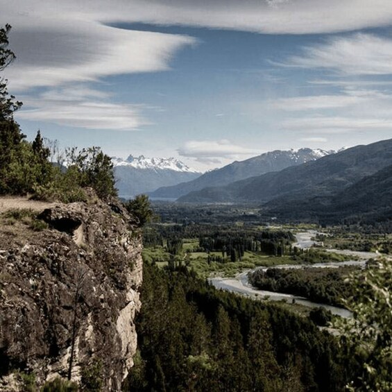 A mountainous landscape with a river, dense forest, and snow-capped peaks. 4