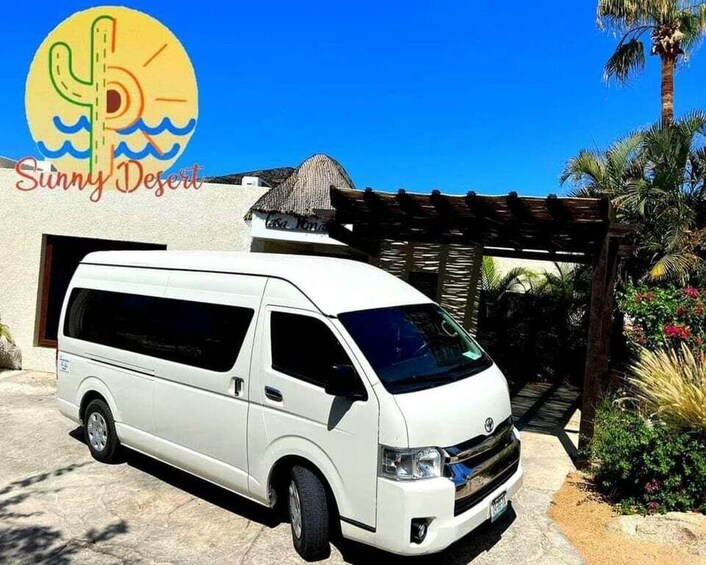 A white van parked in front of a building with a thatched roof, palm trees, and a clear blue sky. 1