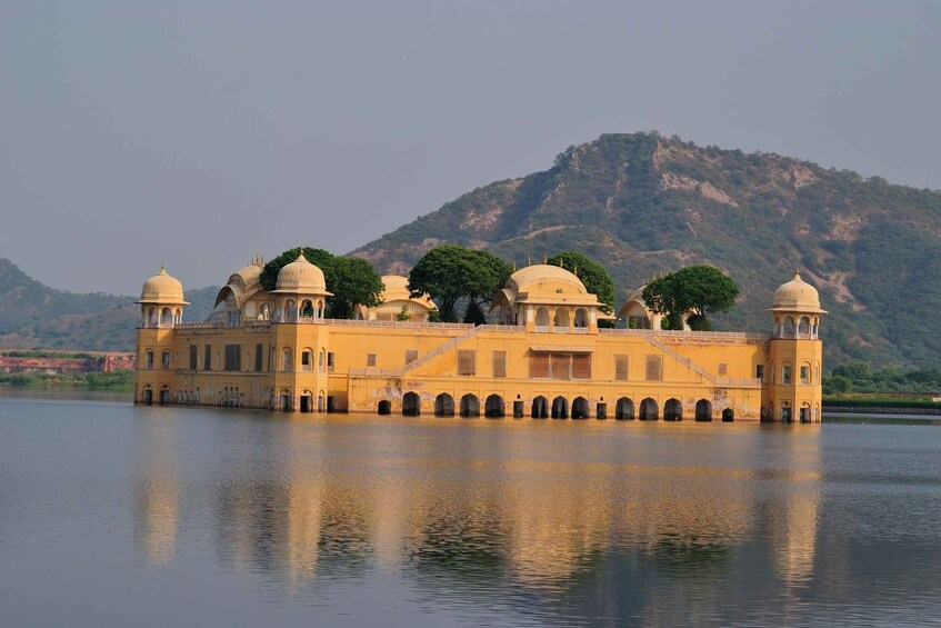 A yellow palace with multiple domes, situated on a lake with a mountainous backdrop. 5