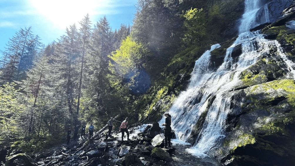 A waterfall in a forest with people standing near it. 3