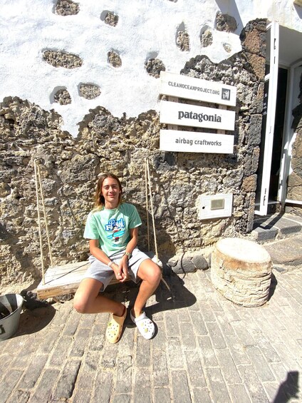 A person sitting on a swing in front of a stone wall with signs for 'Patagonia' and 'airbag craftworks.' 2