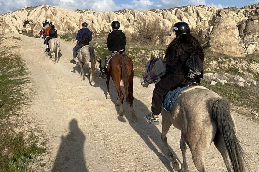 En grupp människor rider på hästar längs en grusväg med stenigt underlag och gles vegetation. 4