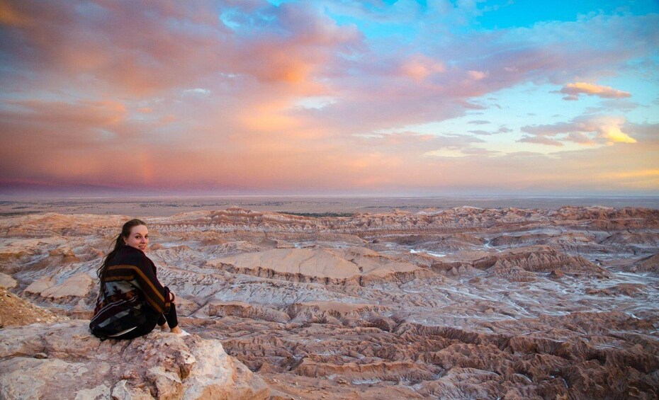 A person sitting on a rocky outcrop overlooking a rugged landscape with layered rock formations. 2