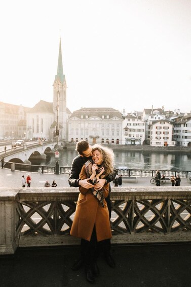 A couple embracing on a bridge with a river and buildings in the background. 1