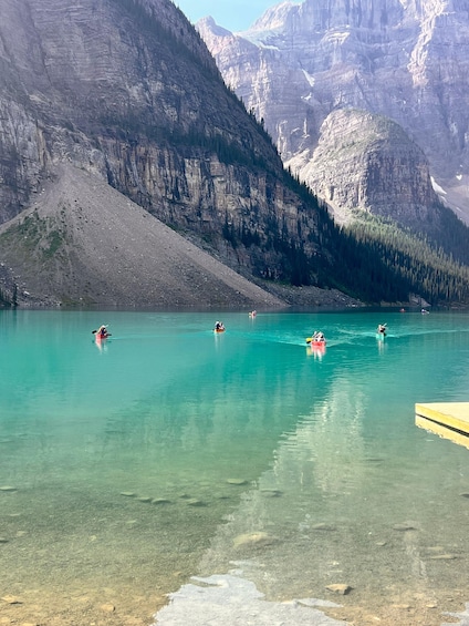 Kayakers on a clear turquoise lake surrounded by mountains. 1